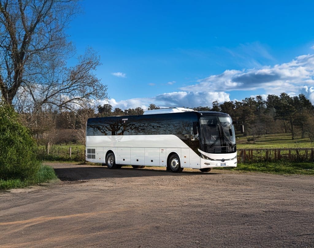 Yutong C12 diesel coach parked on a rural road in Australia with trees, paddocks, and a bright blue sky in the background.